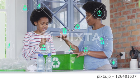 Recycling symbols image over two women sorting plastic bottles in kitchen Recycling symbols image over two women sorting plastic bottles in kitchen 126481637