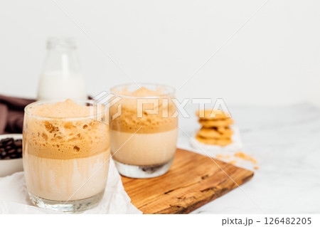 Iced or frappe coffee smoothie on a glass cup and Roasted coffee beans, and milk on marble backdrop. Copy space for your text Iced or frappe coffee smoothie on a glass cup and Roasted coffee beans, and milk on marble backdrop. Copy space for your text 126482205
