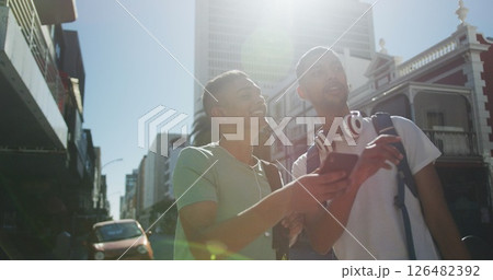 Two happy biracial male friends standing, talking and using smartphone in the street Two happy biracial male friends standing, talking and using smartphone in the street 126482392