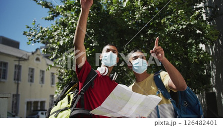 Two biracial male friends wearing face masks using map in the street 126482401