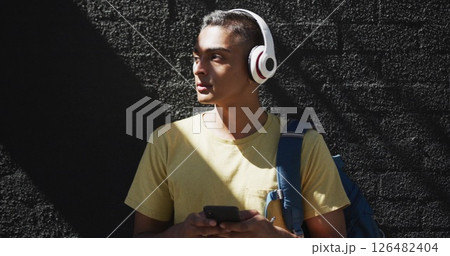 Mid section of biracial man wearing headphones and using smartphone in the street 126482404