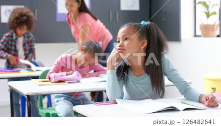 In school, girl daydreaming at desk while classmates and teacher working In school, girl daydreaming at desk while classmates and teacher working 126482641