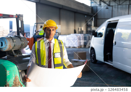 Warehouse worker in safety gear examining blueprint near delivery van 126483458