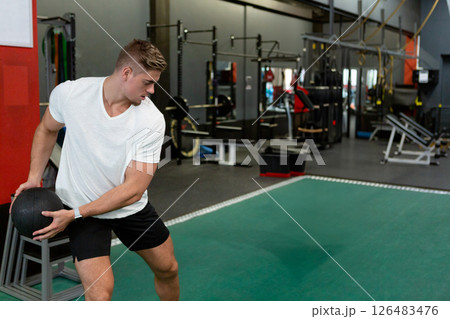 Athletic man exercising with medicine ball in modern gym, focused on fitness, copy space Athletic man exercising with medicine ball in modern gym, focused on fitness, copy space 126483476