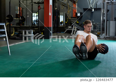 Man exercising with medicine ball on gym floor, focusing on core strength, copy space Man exercising with medicine ball on gym floor, focusing on core strength, copy space 126483477