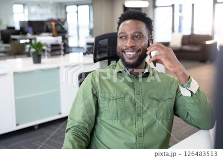Smiling businessman in green shirt talking on smartphone at modern office desk 126483513