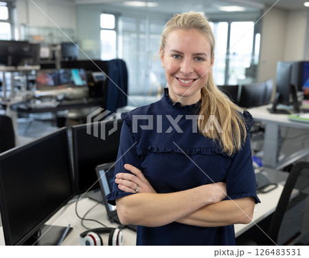 Confident businesswoman standing with arms crossed in modern office workspace 126483531