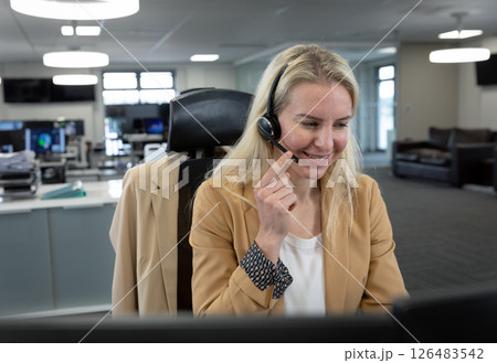 Blonde woman in office using headset, smiling while assisting customer 126483542