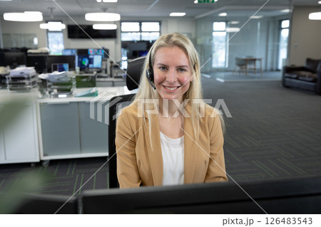 At office desk, businesswoman with headset providing customer support, smiling warmly 126483543