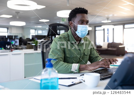 African American man wearing mask typing on keyboard in modern office 126483544