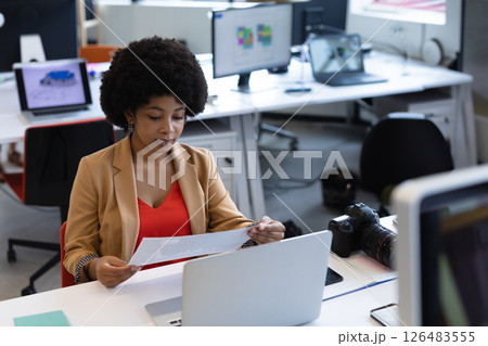Professional woman reviewing documents at office desk with laptop and camera, copy space 126483555