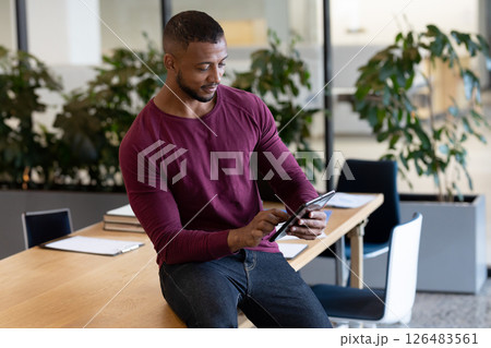 Businessman using tablet while sitting on desk in modern office environment Businessman using tablet while sitting on desk in modern office environment 126483561