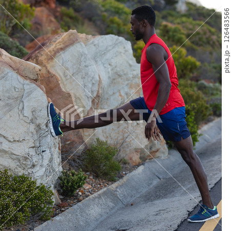 Athletic man stretching leg on rock during outdoor workout in nature 126483566