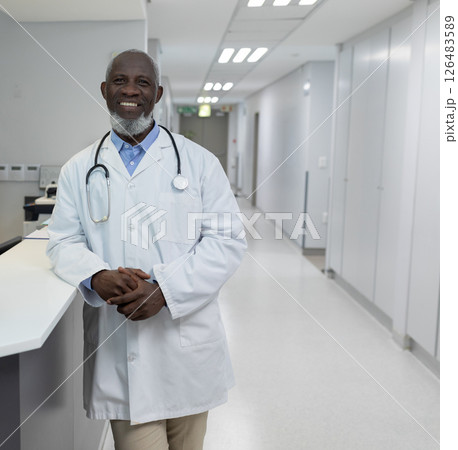 Doctor in white coat smiling confidently in hospital corridor, ready to assist 126483589