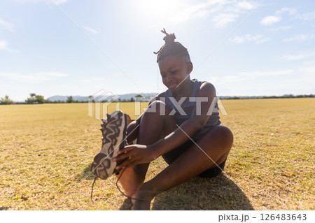 African American girl tying shoelaces on field, preparing for outdoor activity African American girl tying shoelaces on field, preparing for outdoor activity 126483643