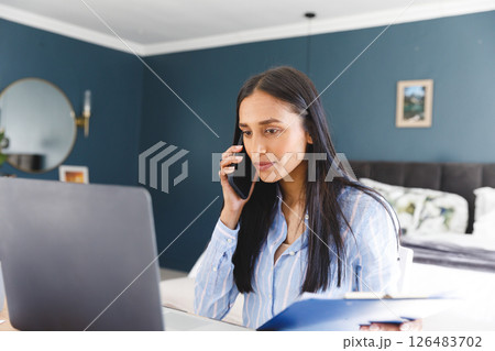 Working from home, woman using laptop and talking on smartphone in bedroom 126483702