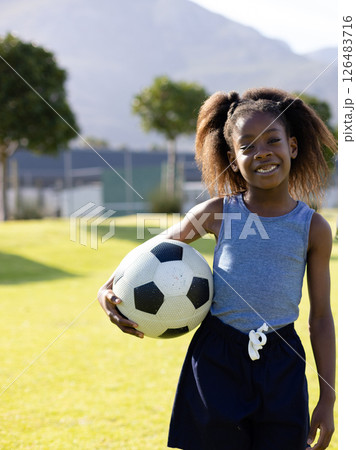 Smiling girl holding soccer ball on school field, enjoying sunny day outdoors, copy space 126483716