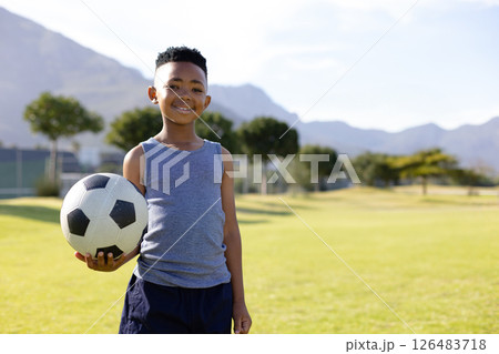 Smiling boy holding soccer ball on school field with mountains in background, copy space 126483718
