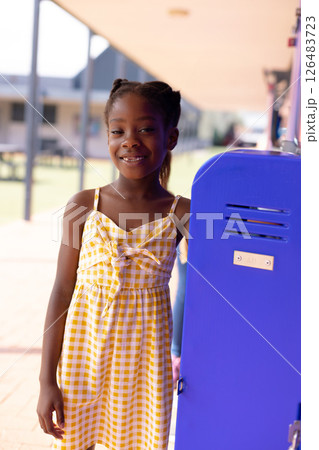 Smiling girl standing by blue locker outside school, enjoying sunny day 126483723