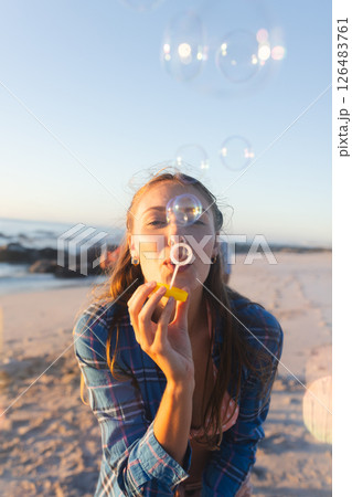 Young woman blowing bubbles on beach at sunset, enjoying carefree moment Young woman blowing bubbles on beach at sunset, enjoying carefree moment 126483761