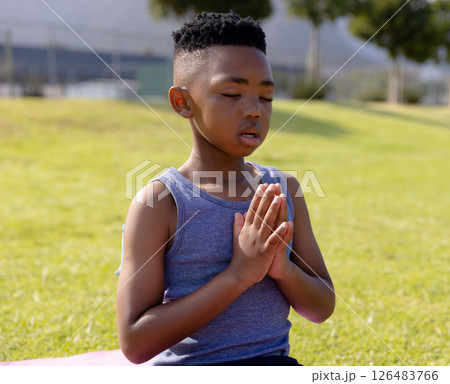 Young boy meditating outdoors on grass, focusing with hands in prayer position 126483766
