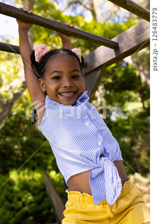 Smiling girl playing on monkey bars in park, enjoying sunny day outdoors 126483779