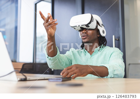 Using VR headset and laptop, African American man interacting virtually in office Using VR headset and laptop, African American man interacting virtually in office 126483793