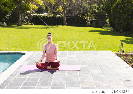 Woman meditating on yoga mat by pool, enjoying peaceful outdoor setting, copy space 126483826