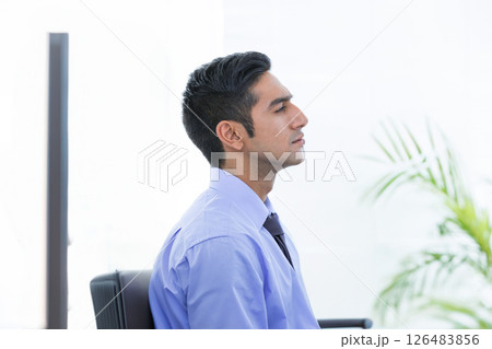Businessman in blue shirt relaxing at office desk, taking deep breath Businessman in blue shirt relaxing at office desk, taking deep breath 126483856