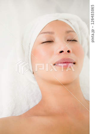 Receiving facial treatment, serene asian woman with towel wrapped head relaxing at spa Receiving facial treatment, serene asian woman with towel wrapped head relaxing at spa 126483865