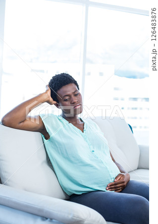 Pregnant african american woman relaxing on sofa, gently touching belly, looking thoughtful Pregnant african american woman relaxing on sofa, gently touching belly, looking thoughtful 126483876