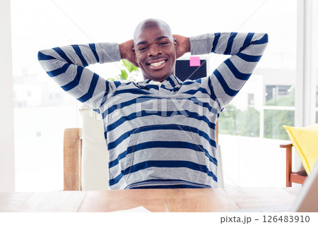 Smiling man in striped hoodie relaxing at office desk, feeling content 126483910