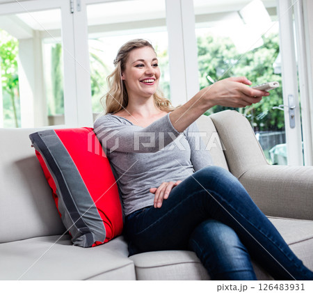 Smiling woman relaxing on sofa, using remote control at home, enjoying leisure time 126483931