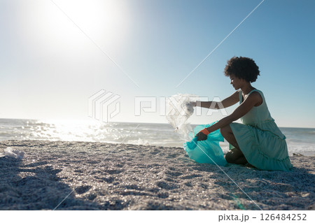 African American woman cleaning beach, collecting plastic waste under bright sun, copy space African American woman cleaning beach, collecting plastic waste under bright sun, copy space 126484252