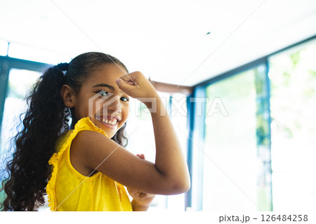 Smiling girl in yellow dress flexing arm, showing strength and confidence, copy space 126484258