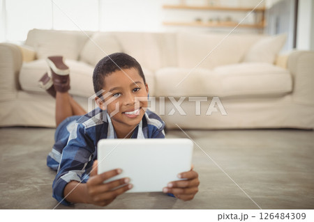 Smiling boy using tablet on living room floor, enjoying leisure time at home, copy space 126484309