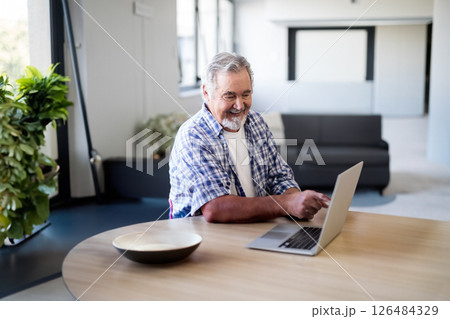 Senior man using laptop at home, smiling and enjoying leisure time Senior man using laptop at home, smiling and enjoying leisure time 126484329