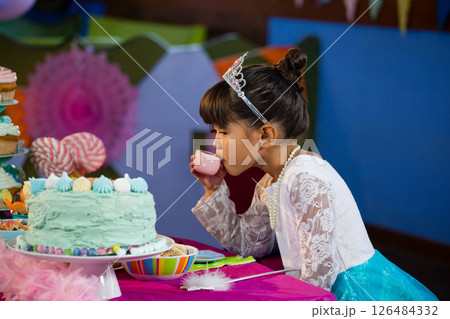 Young girl in princess dress sipping tea at colorful birthday party table, copy space Young girl in princess dress sipping tea at colorful birthday party table, copy space 126484332