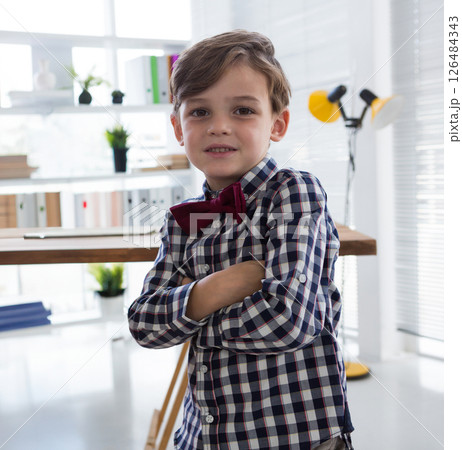 Confident boy in checkered shirt crossing arms in modern office setting 126484343