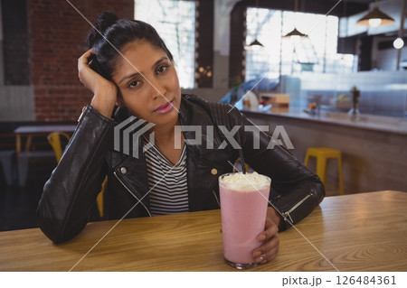 Woman in leather jacket enjoying strawberry milkshake at trendy cafe table Woman in leather jacket enjoying strawberry milkshake at trendy cafe table 126484361