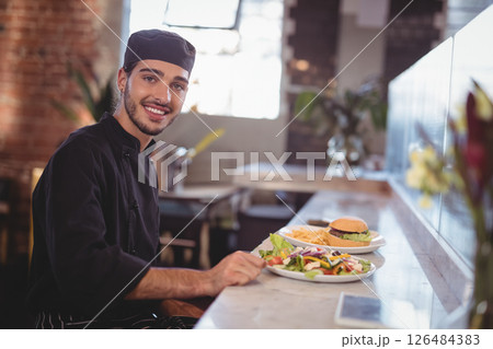Smiling chef presenting delicious salad and burger at modern cafe counter, copy space 126484383