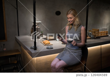 Smiling woman enjoying coffee and checking smartphone at modern kitchen counter, copy space Smiling woman enjoying coffee and checking smartphone at modern kitchen counter, copy space 126484389