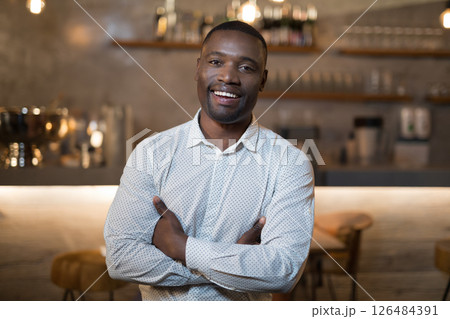 Smiling man in restaurant standing confidently with arms crossed, enjoying evening 126484391