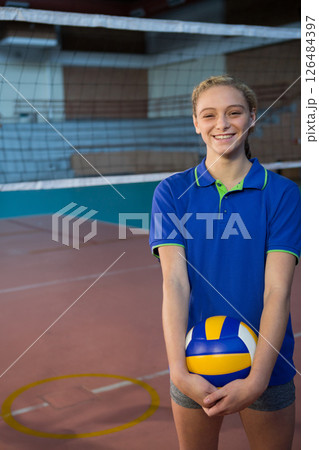 Teen girl holding volleyball, smiling confidently on indoor court, ready to play, copy space 126484397