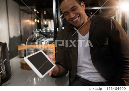 Smiling man holding tablet at modern restaurant, enjoying evening dining experience, copy space 126484400