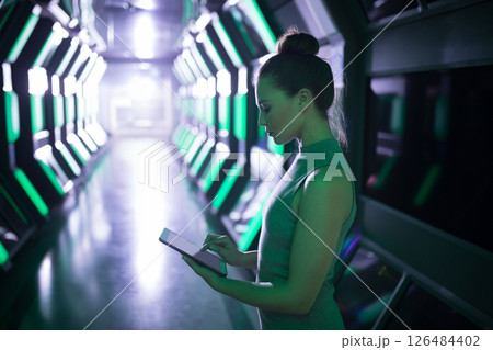 Woman using tablet in futuristic office corridor, focused on digital tasks, copy space 126484402