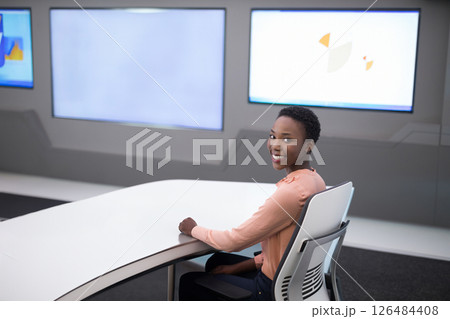 Smiling woman sitting at modern desk in high-tech office environment, copy space 126484408