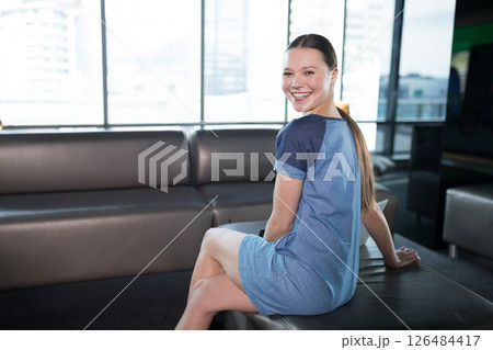 Smiling woman in modern office wearing casual dress, sitting on sofa, copy space Smiling woman in modern office wearing casual dress, sitting on sofa, copy space 126484417