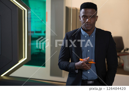 Businessman holding pen standing confidently in modern futuristic office environment, copy space Businessman holding pen standing confidently in modern futuristic office environment, copy space 126484420
