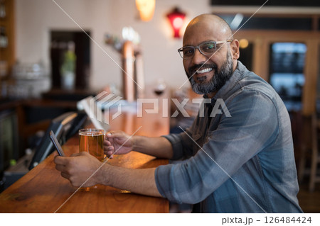 Smiling man enjoying beer and using smartphone at cozy bar counter, copy space 126484424